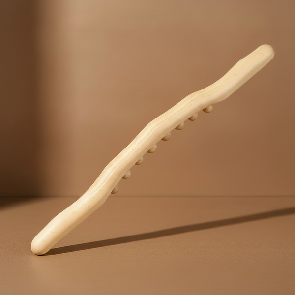 Bâton de massage en hêtre clair, une seule rangée de billes de bois sculptées, posé contre un mur caramel