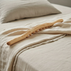 Bâton de massage en hêtre posé sur un plaid en lin, sur un lit, entre deux séances